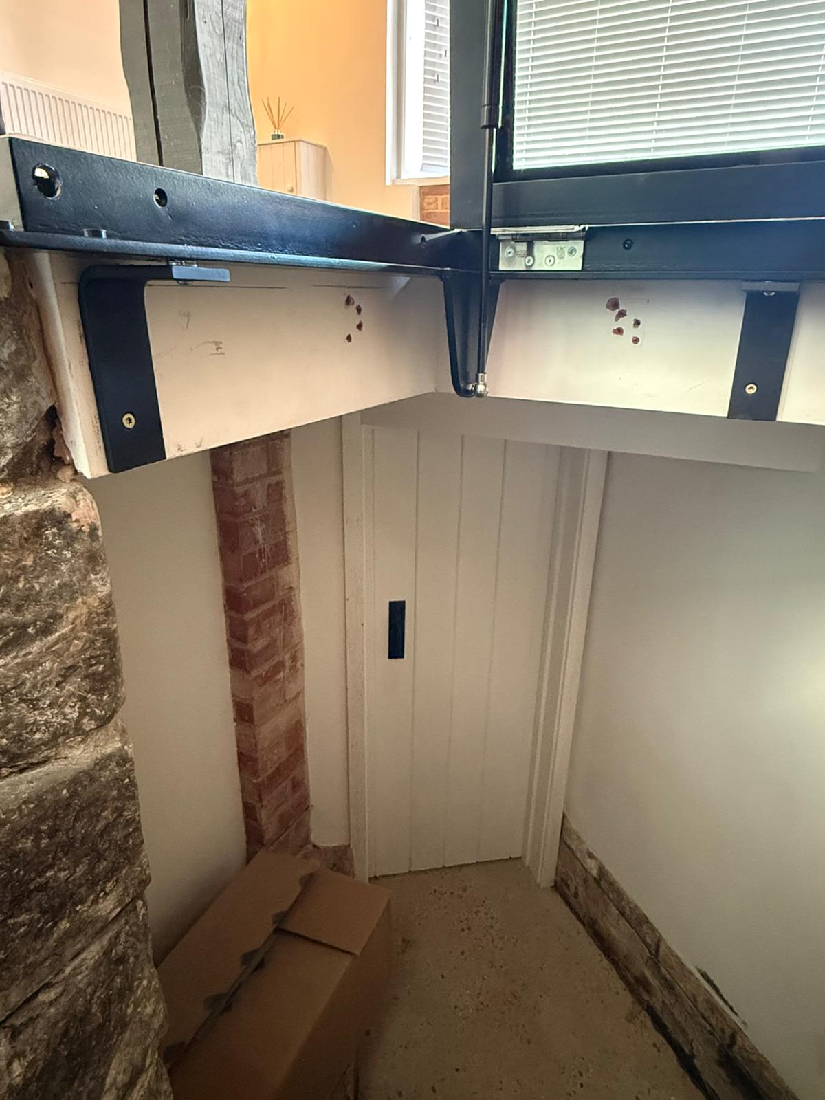 Underside of hinged glass floor showing powder coated steel frame and bracket fixing into stone wall, Burwash